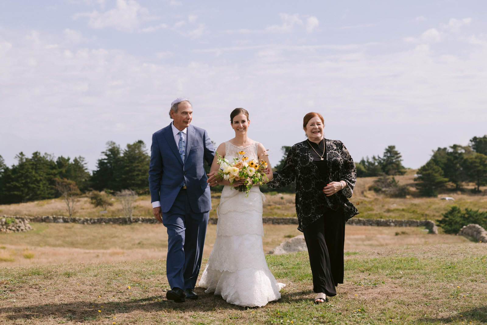 Sarah being walked down the aisle of her wedding with her two parents at her outdoor block island wedding.