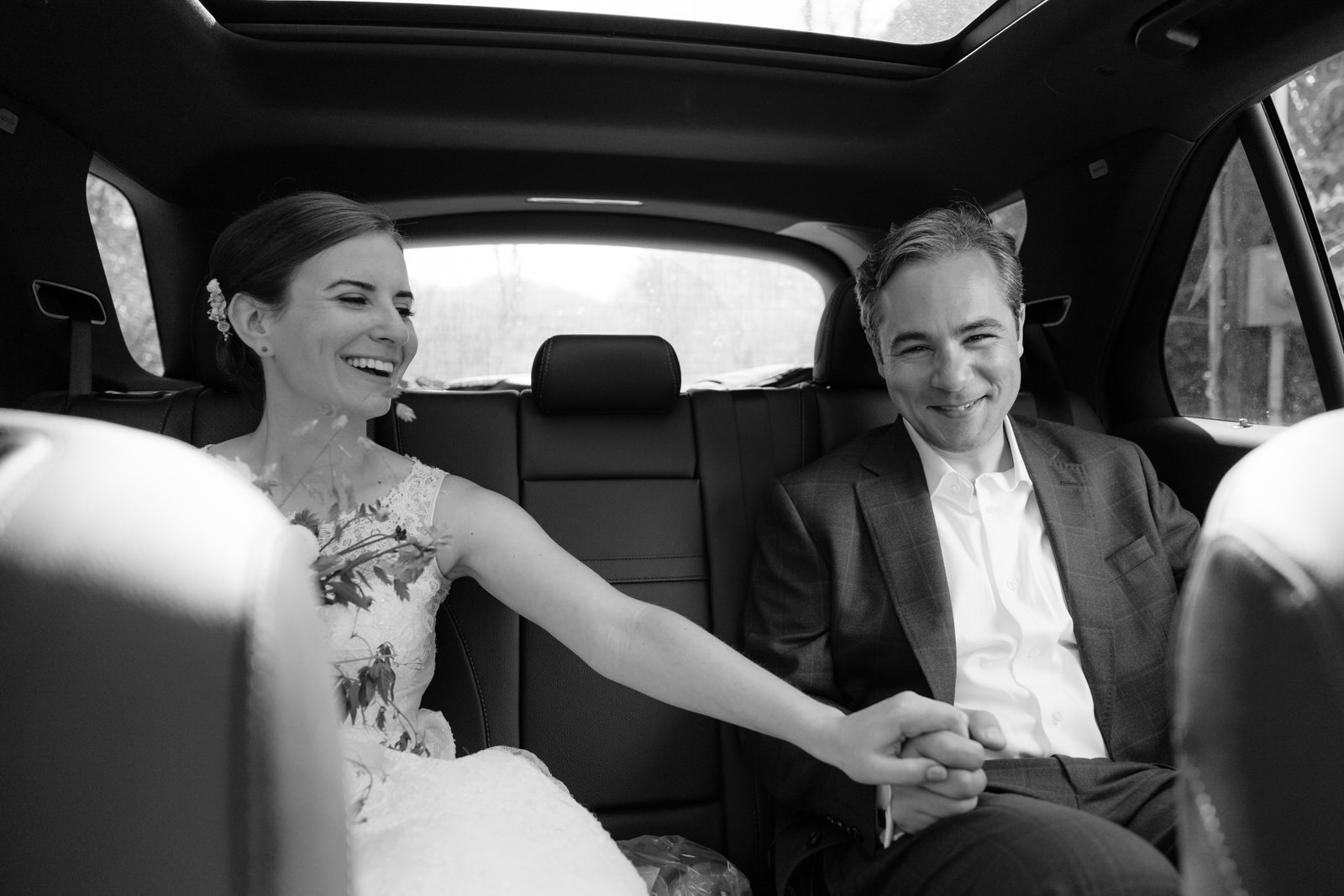 sarah and jason traveling to their reception. Couple holding hands in the backseat.